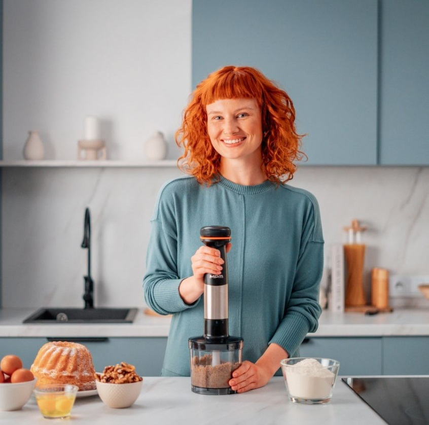Kobieta z rudymi włosami trzyma blender ręczny w kuchni ze składnikami.