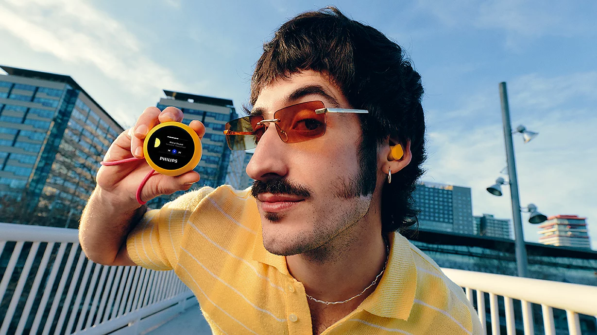 Ein Mann mit Schnurrbart und Sonnenbrille hält einen gelben MP3-Player.