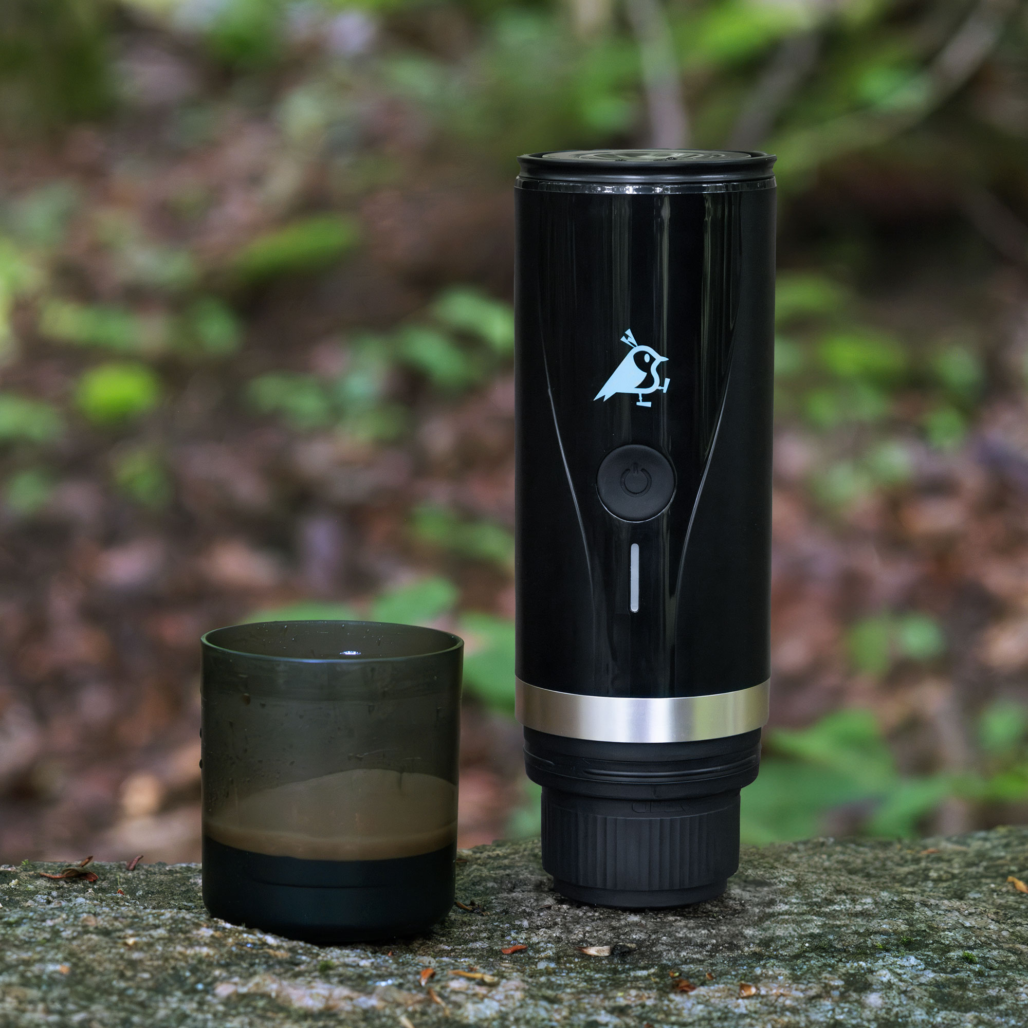 Ein schwarzer Kaffeezubereiter mit einer Tasse auf einem Stein im Wald.