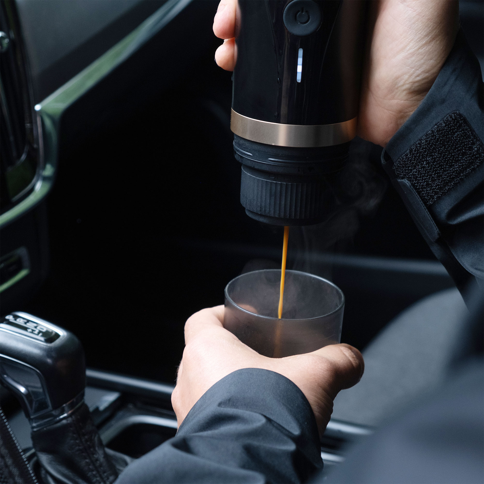 Eine Person brüht Kaffee in einem Auto, der Kaffee fließt in ein Glas.