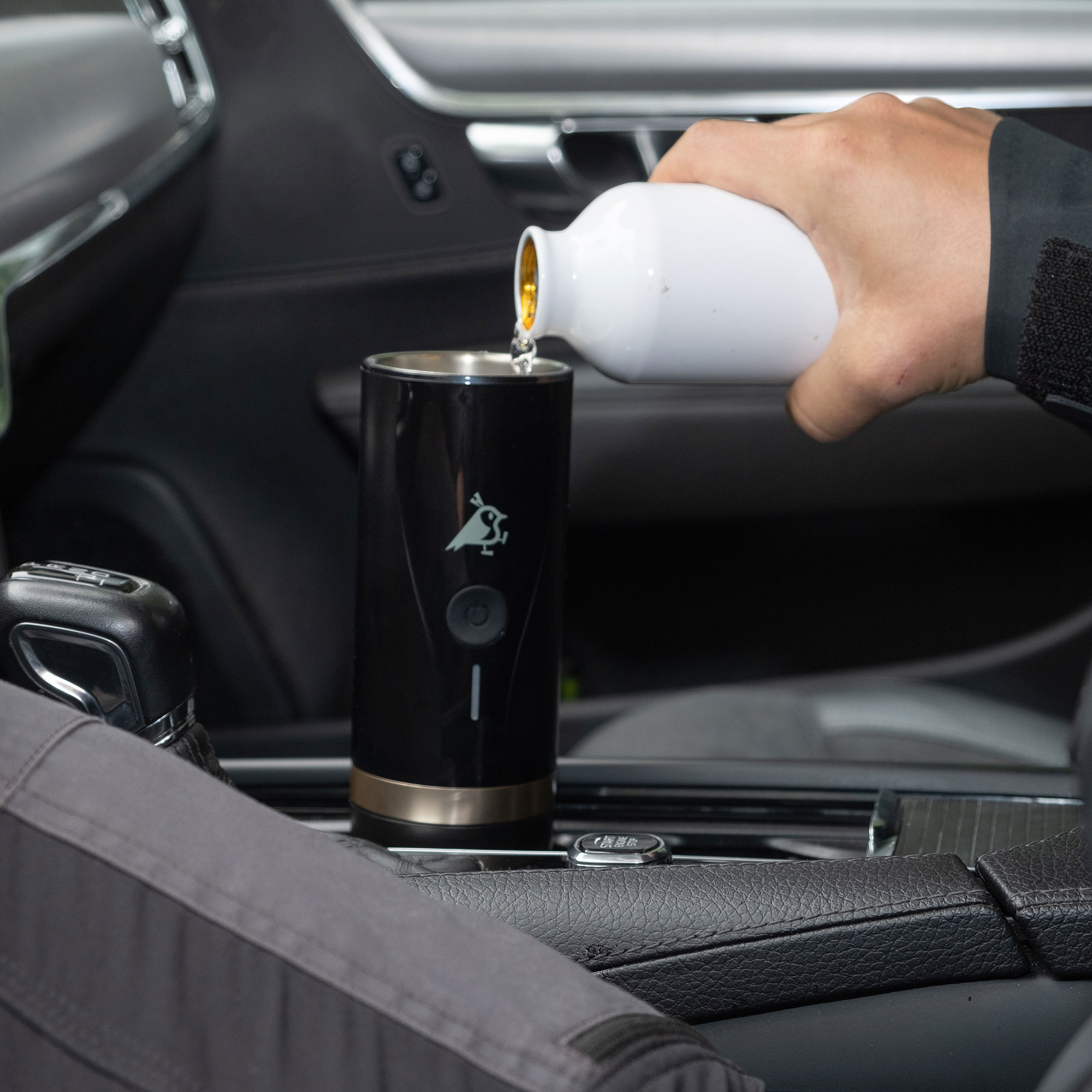 Eine Hand gießt Flüssigkeit aus weißer Flasche in schwarzen Becher im Auto.