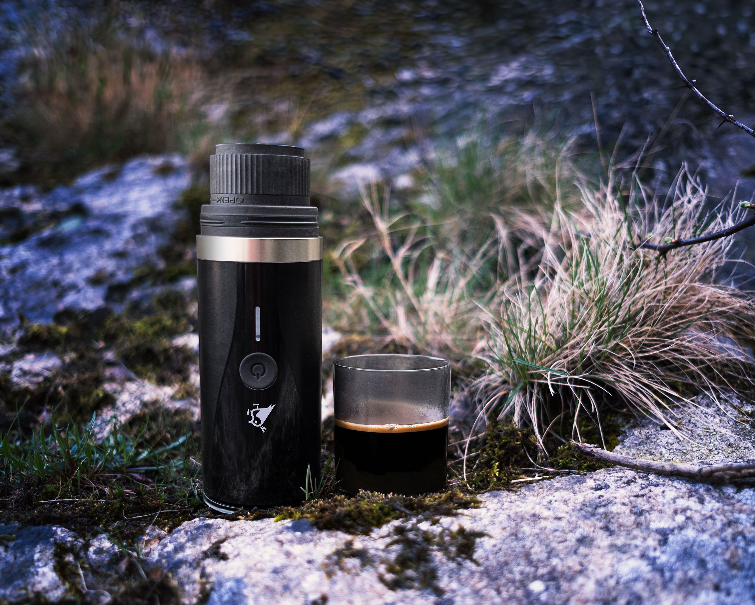 Ein schwarzer Kaffeezubereiter und ein Glas Espresso stehen auf Felsen im Freien.