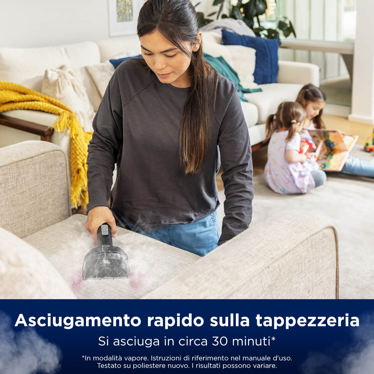 Una donna pulisce un divano con un pulitore a vapore mentre i bambini leggono sullo sfondo.