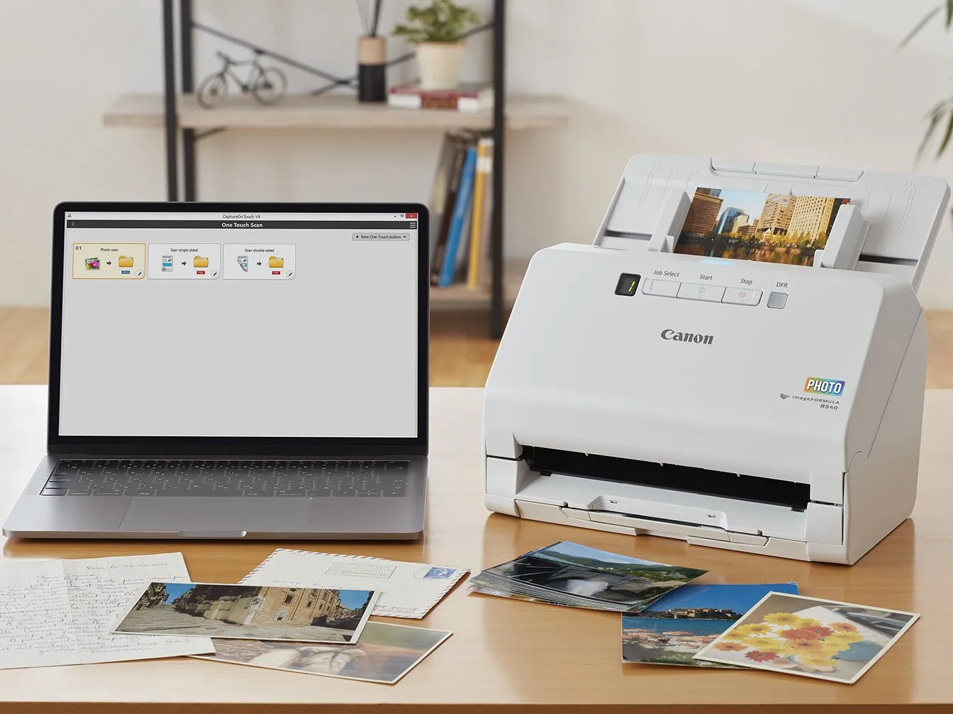 Uno scanner Canon e un laptop su una scrivania di legno, con foto e documenti.