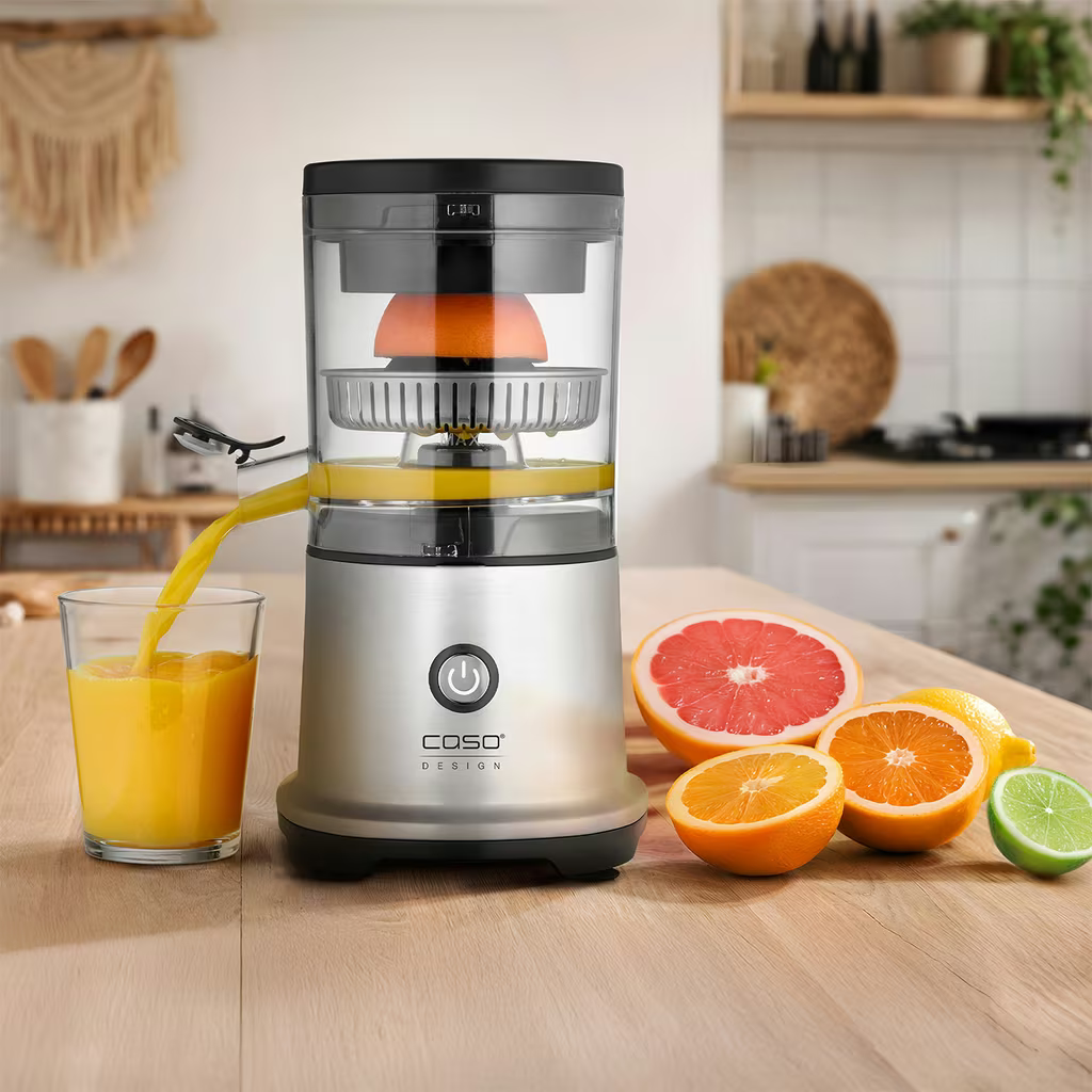 Elektrische Zitruspresse mit Saft im Glas und Früchten daneben.
