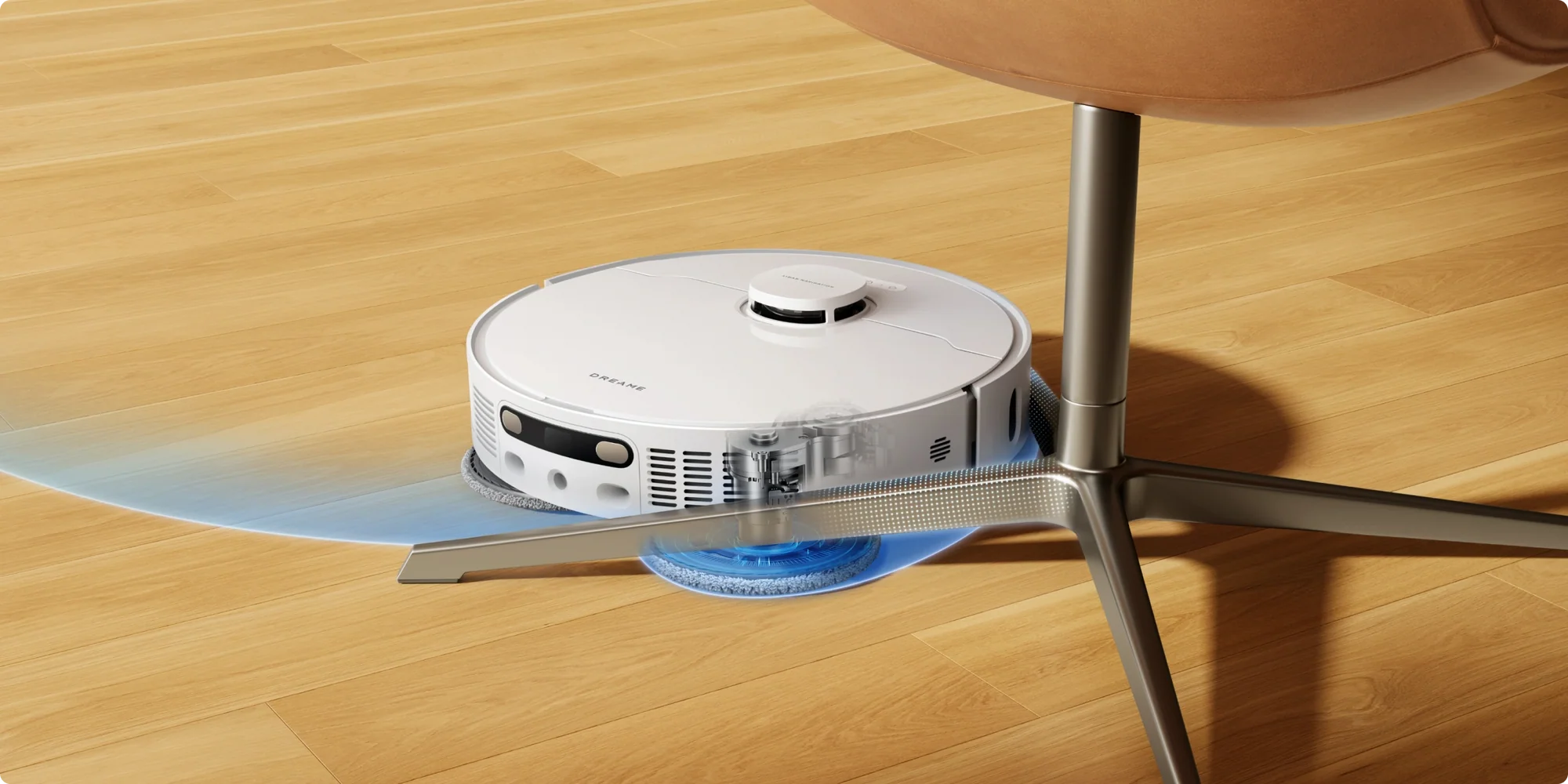 Egy fehér robotporszívó tisztít egy fa padlót egy barna szék alatt.