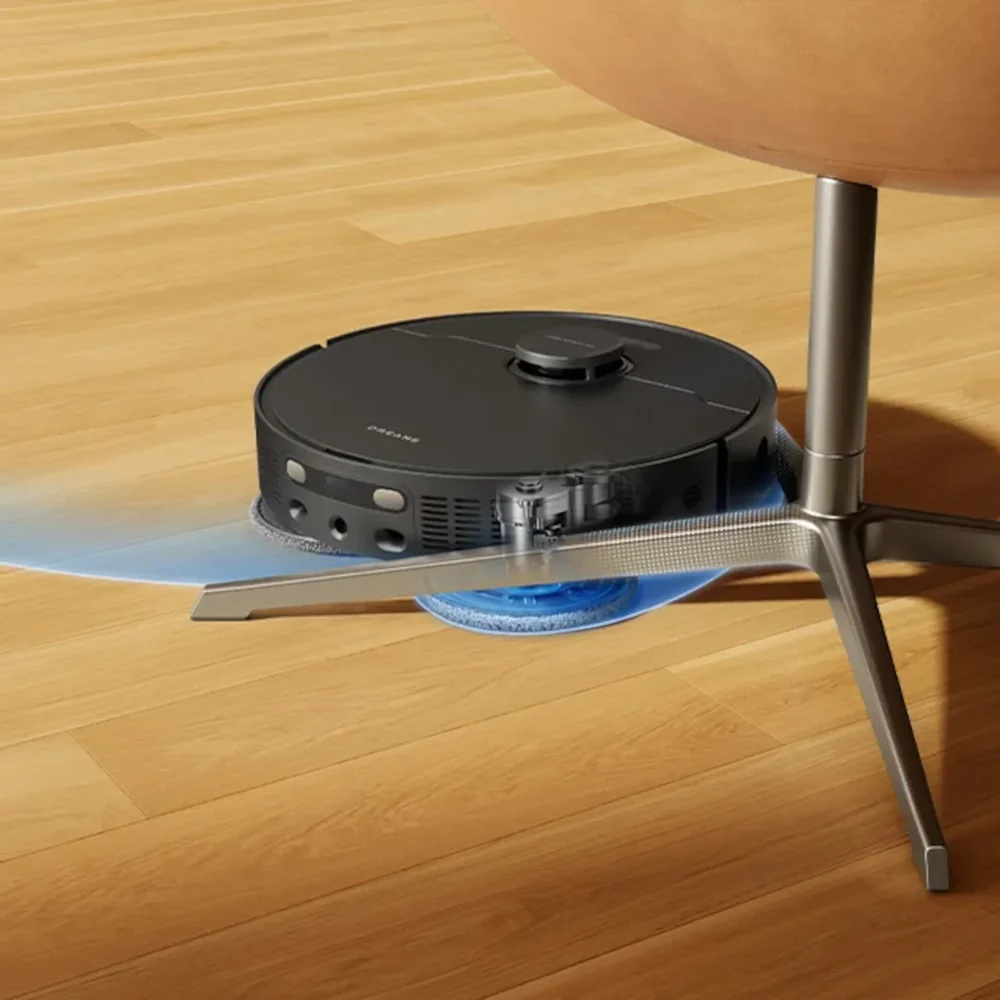 Egy fekete robotporszívó tisztít egy szék alatt egy fapadlón.