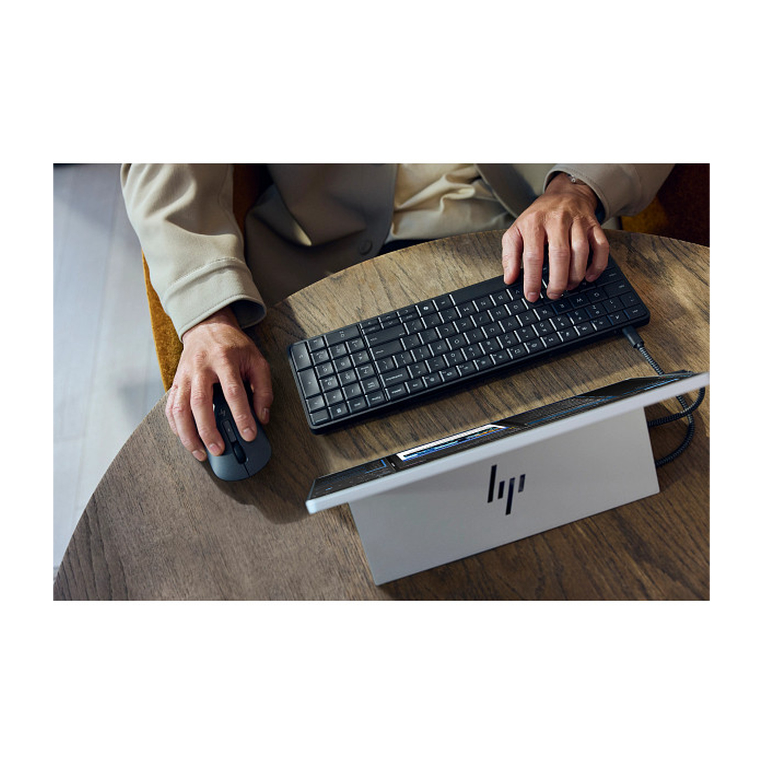 Persona che usa un mouse e una tastiera su un tavolo di legno accanto a un laptop.