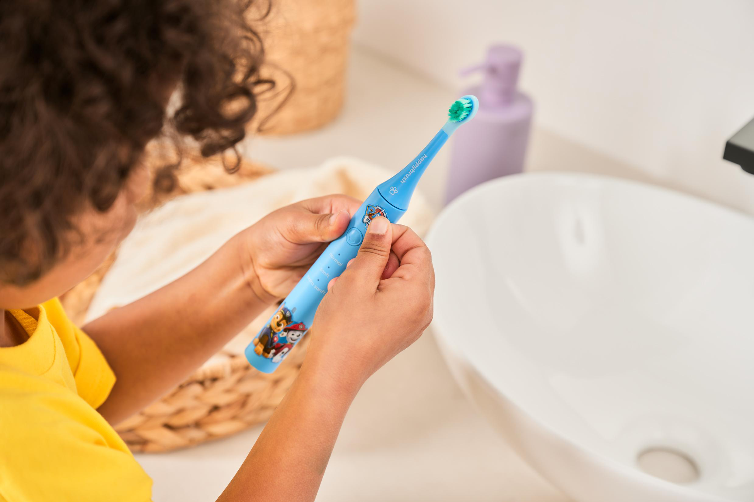 Ein Kind hält eine blaue Zahnbürste mit Paw Patrol-Motiv in einem Badezimmer.