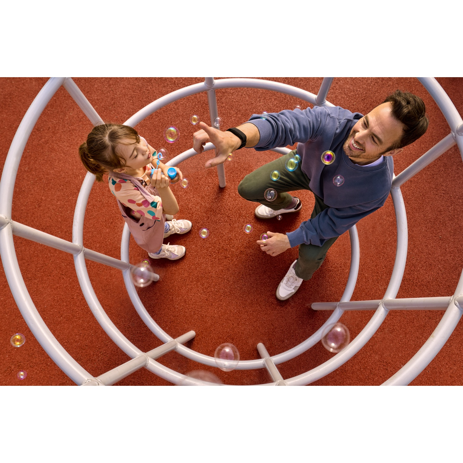 Man en kind spelen met bellen op een rode speelplaats.
