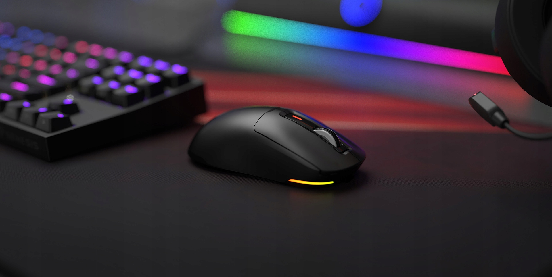 Czarna mysz gamingowa z podświetleniem RGB stoi na biurku obok klawiatury.