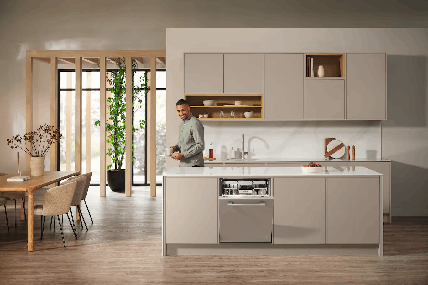 Hombre en cocina moderna con lavavajillas abierto, sosteniendo una taza.