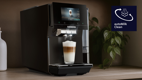 Yanında bir bardak latte macchiato bulunan siyah kahve makinesi.