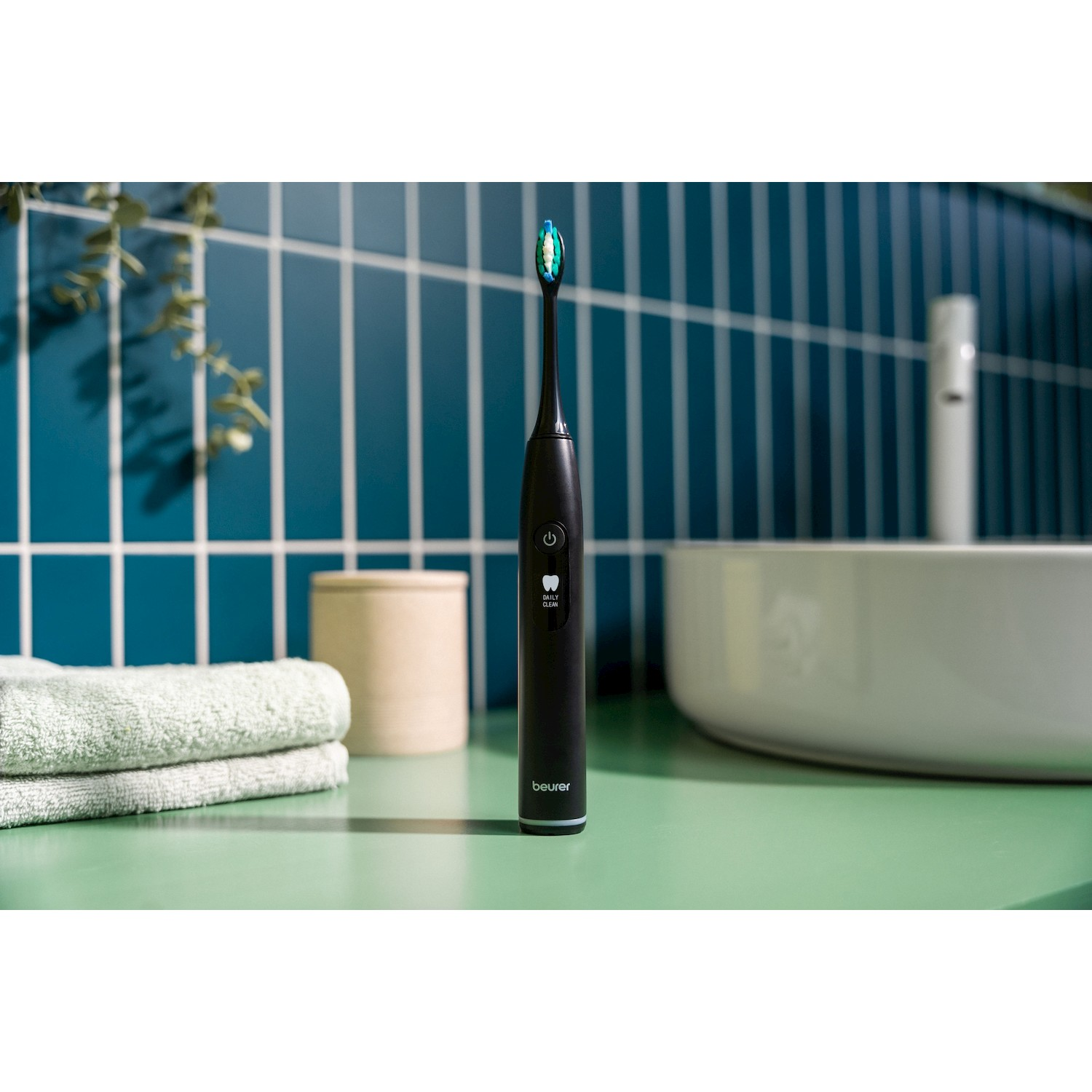 Spazzolino elettrico nero con setole blu e verdi, su un piano verde.