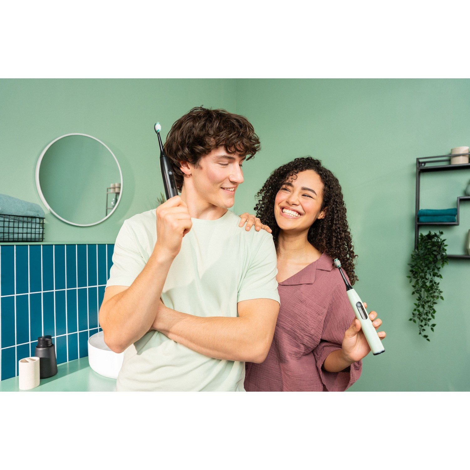Un uomo e una donna sorridono tenendo spazzolini in un bagno.