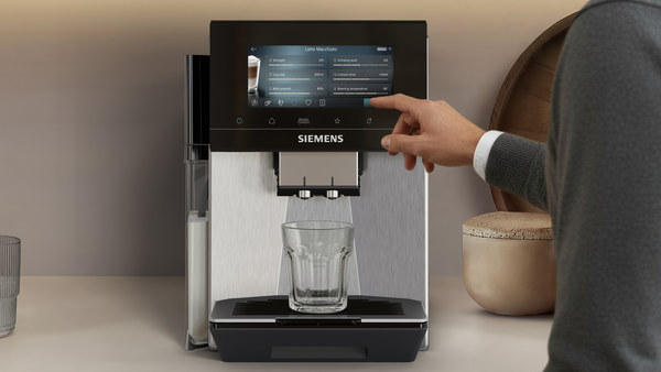 Bir adam latte macchiato yapmak için dokunmatik ekranlı kahve makinesini çalıştırıyor.