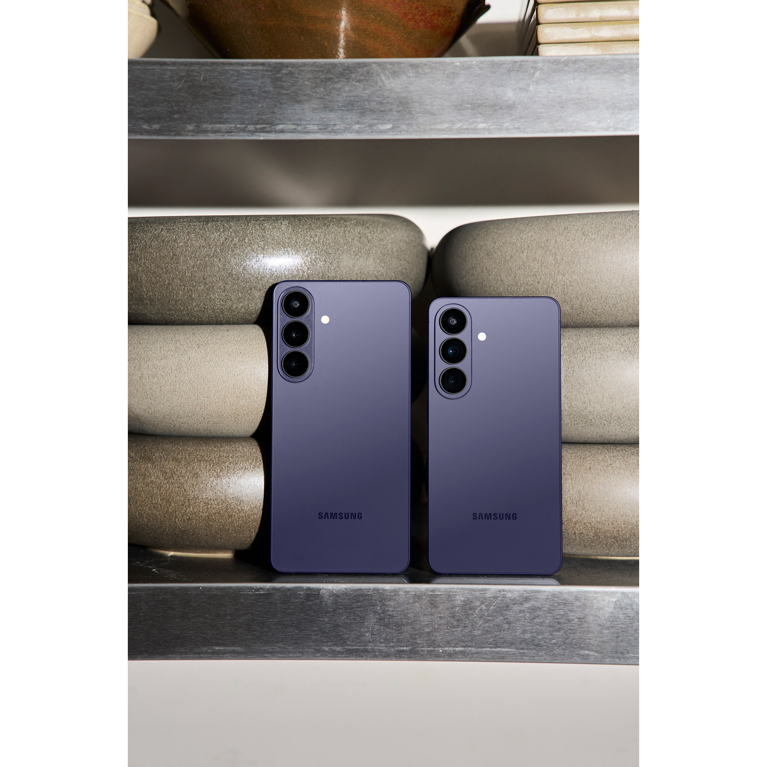 Twee paarse Samsung telefoons op een plank met keramische kommen.