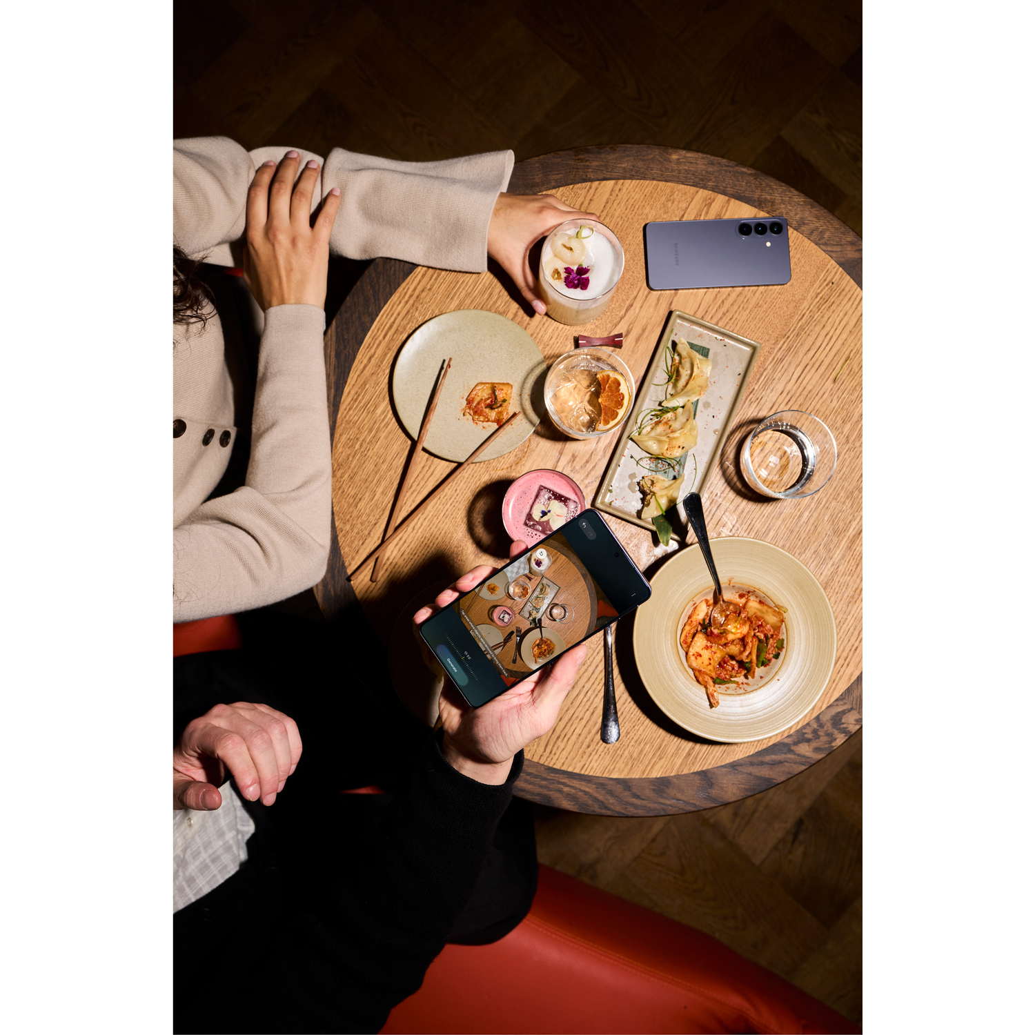 Twee personen aan tafel met eten en drinken. Eén fotografeert het eten met een telefoon.