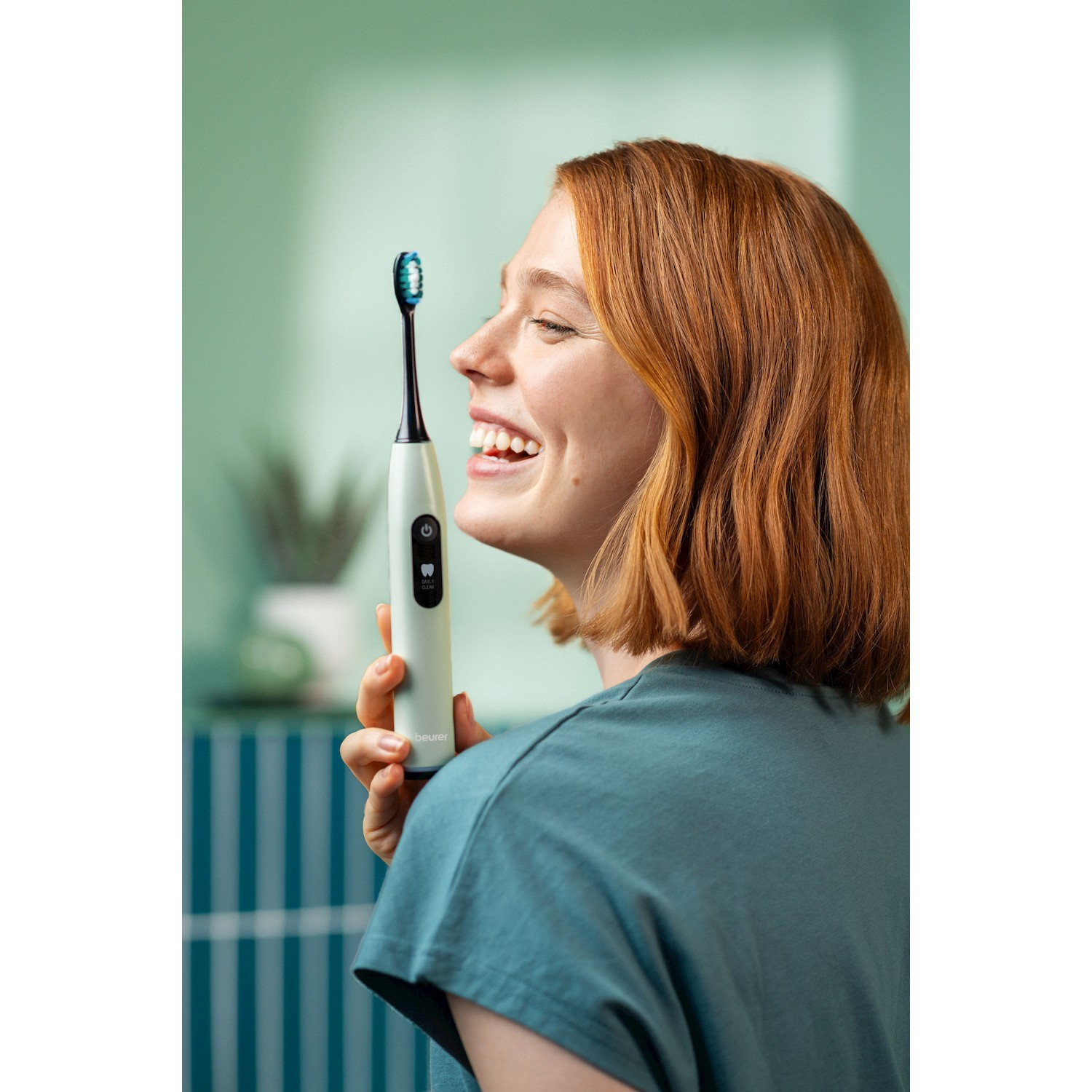 Una donna dai capelli rossi ride tenendo uno spazzolino elettrico.
