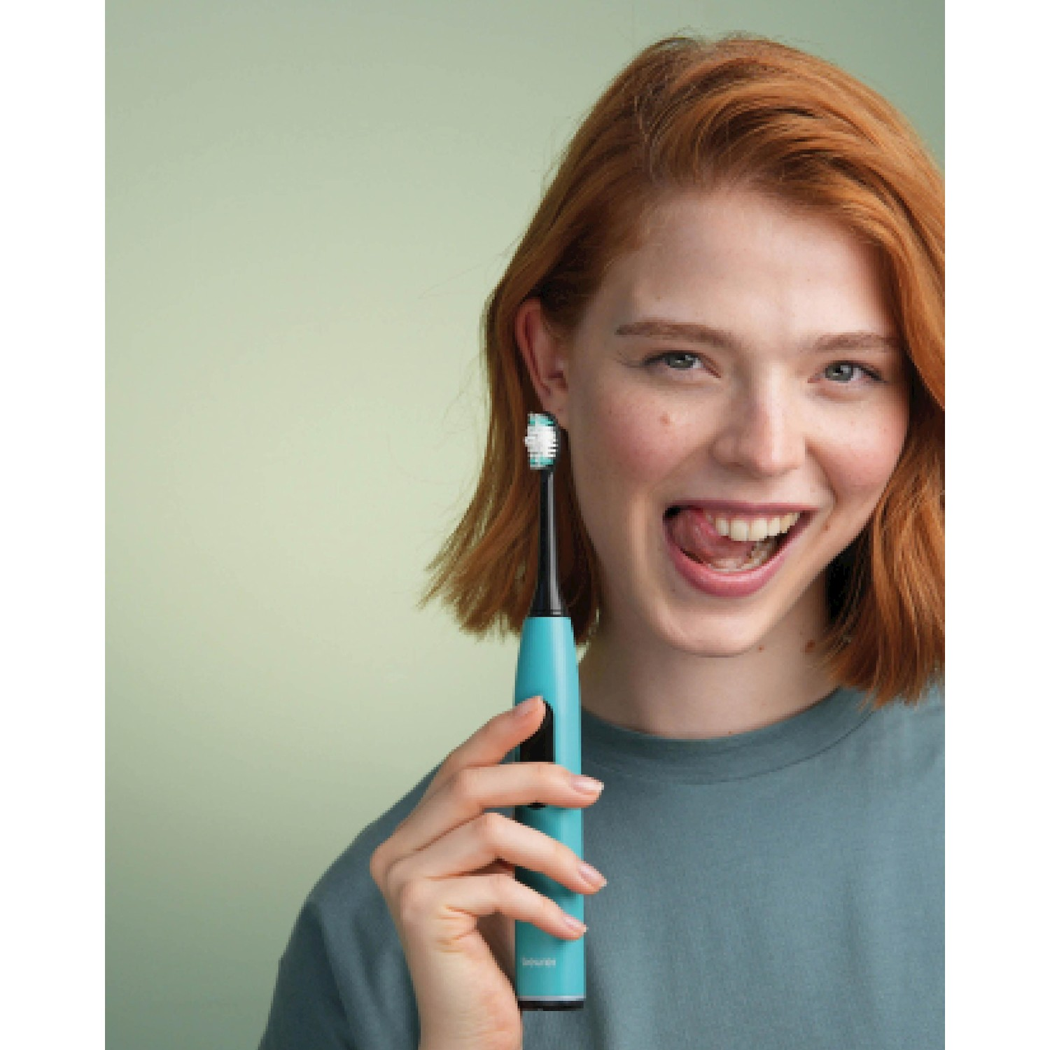 Una donna dai capelli rossi tiene uno spazzolino blu e tira fuori la lingua.