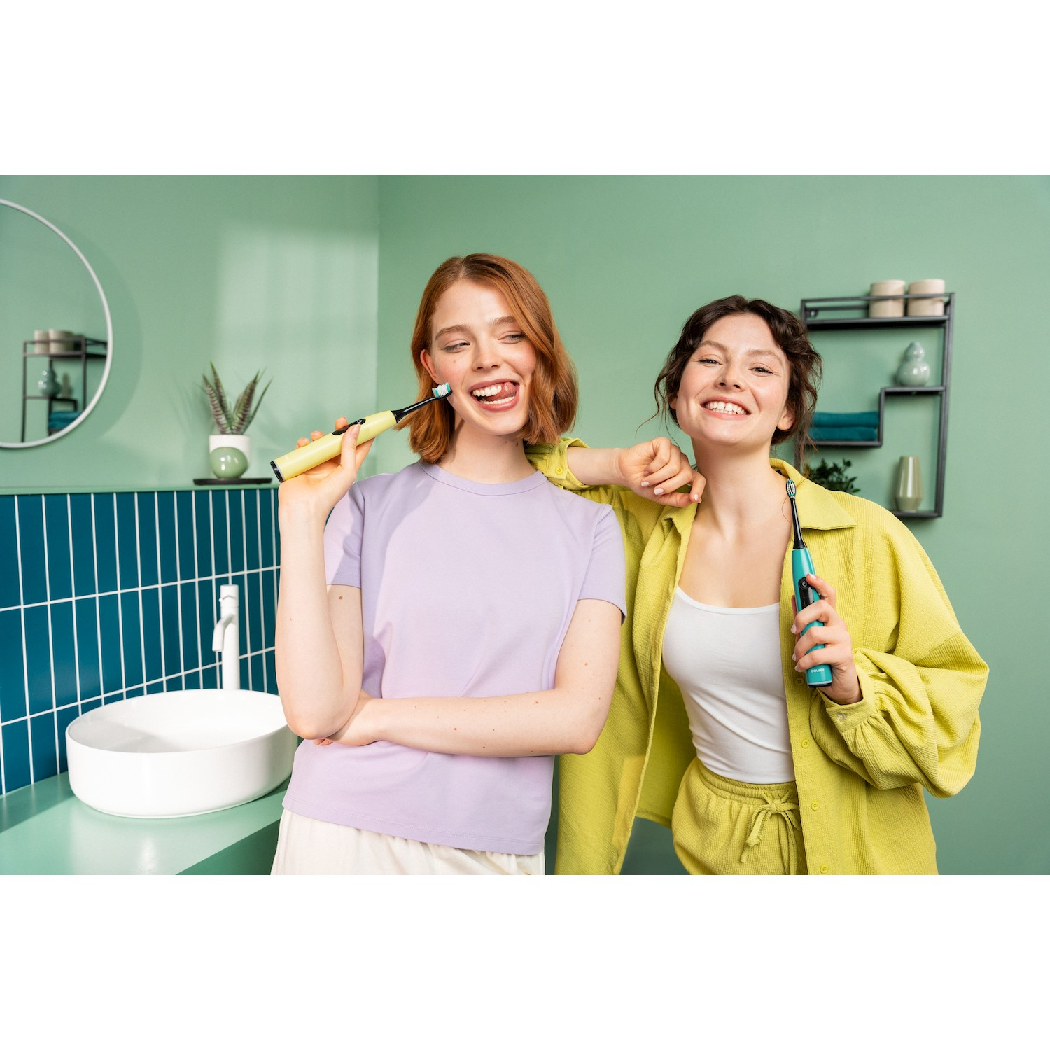 Due donne con spazzolini elettrici in un bagno verde.