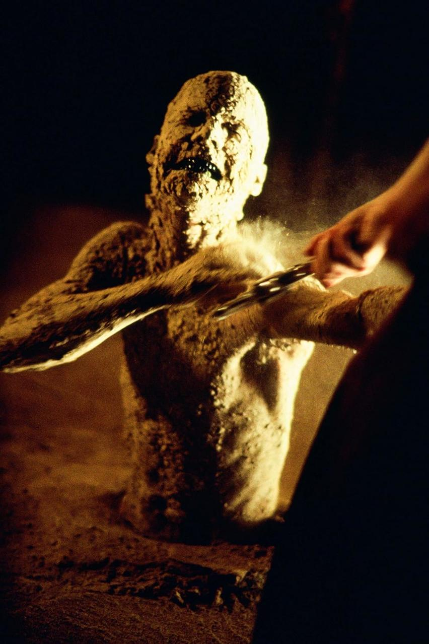 Eine aus Sand oder Ton bestehende Gestalt windet sich, während Staub aufgewirbelt wird.