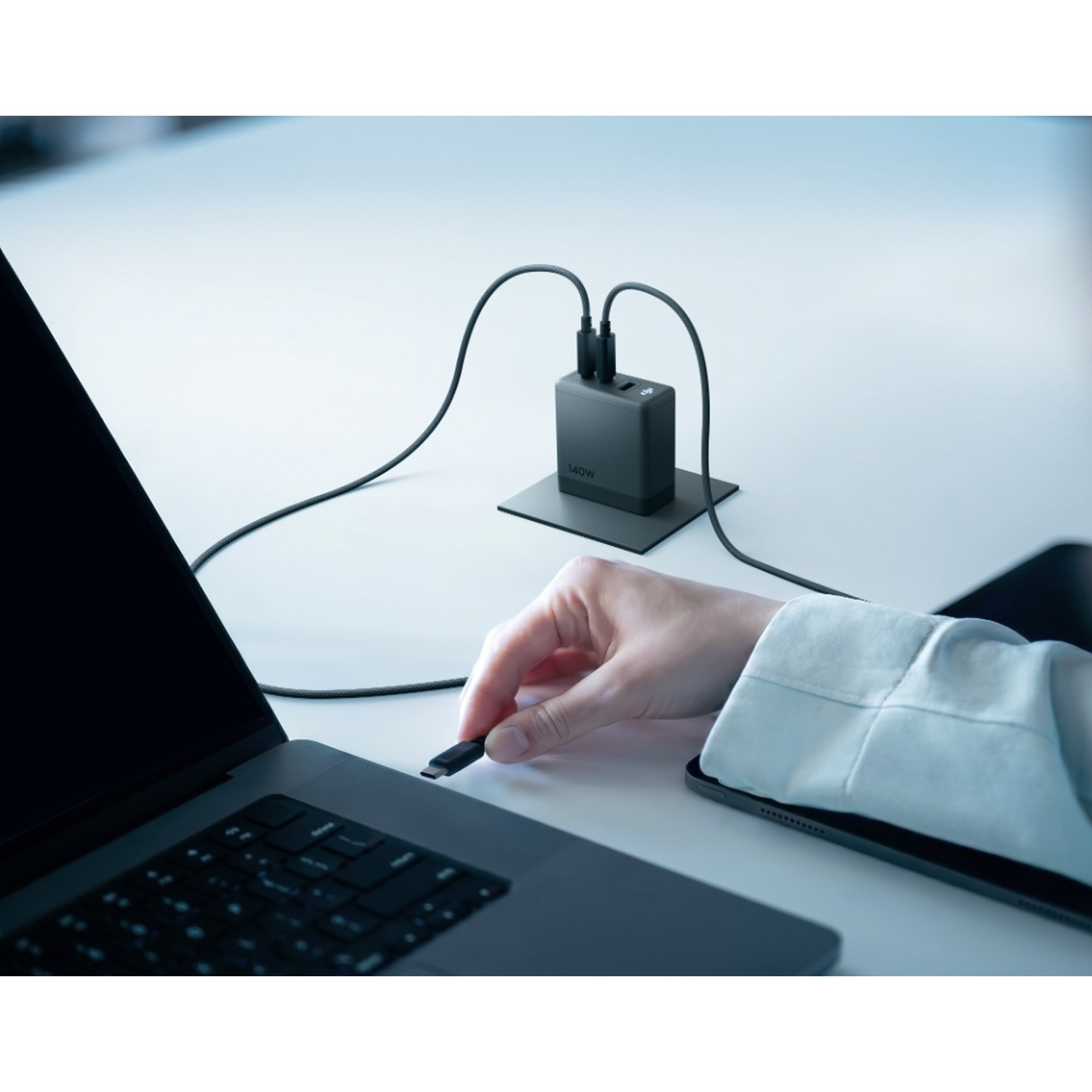 Una mano collega un cavo USB-C a un laptop, con un caricabatterie da 140W sulla scrivania.