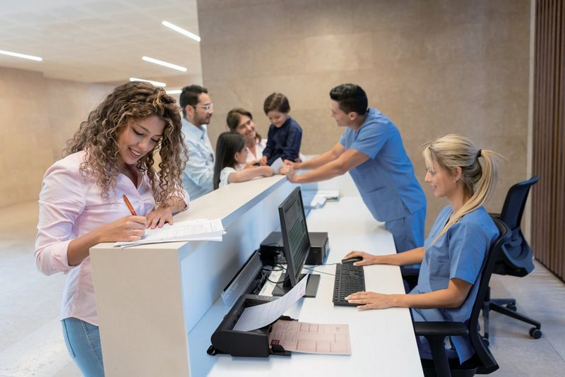 Una donna scrive alla reception dell'ospedale mentre una famiglia e il personale medico aspettano.