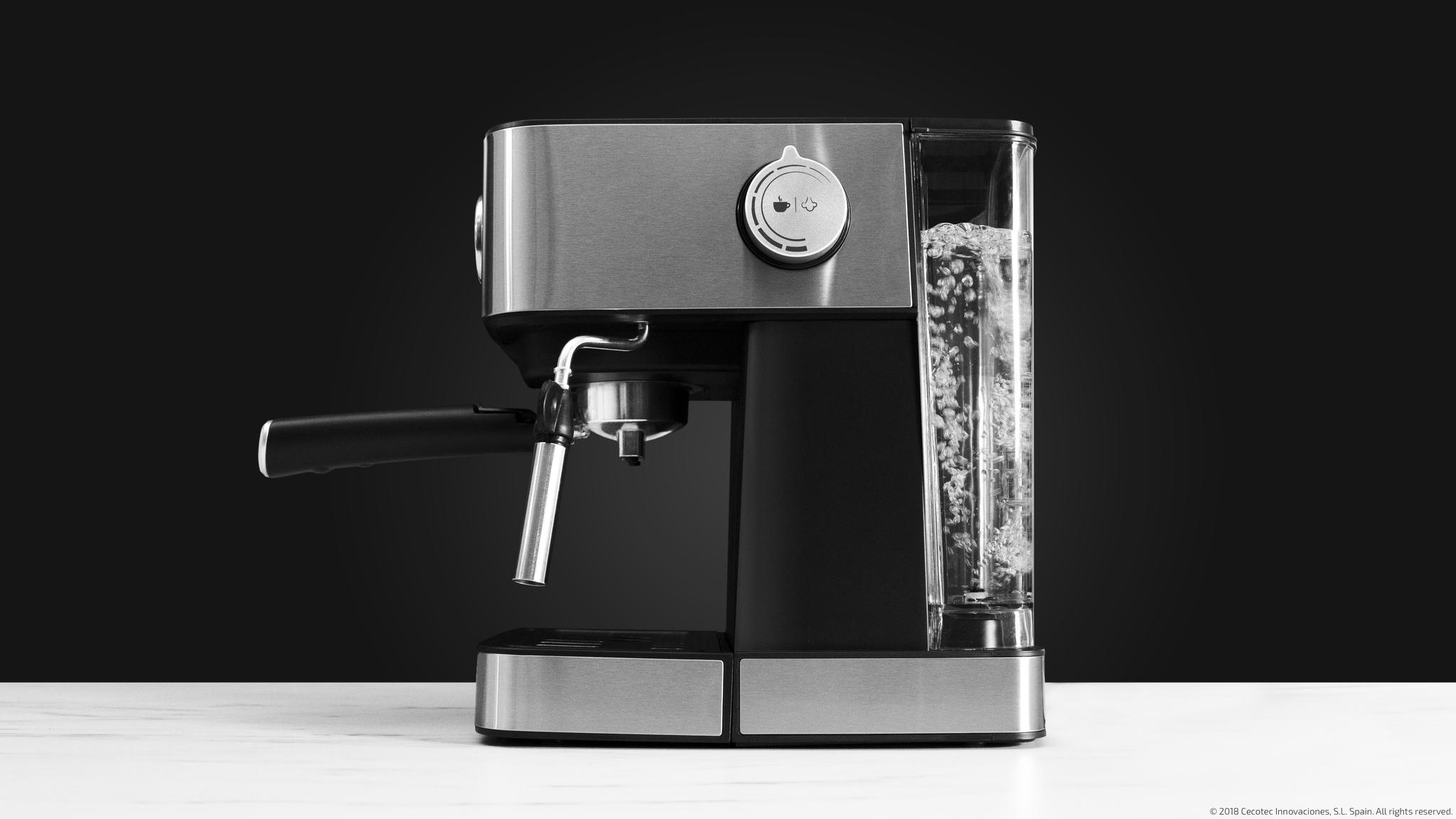 Una cafetera de acero inoxidable con depósito de agua sobre una mesa y fondo negro.