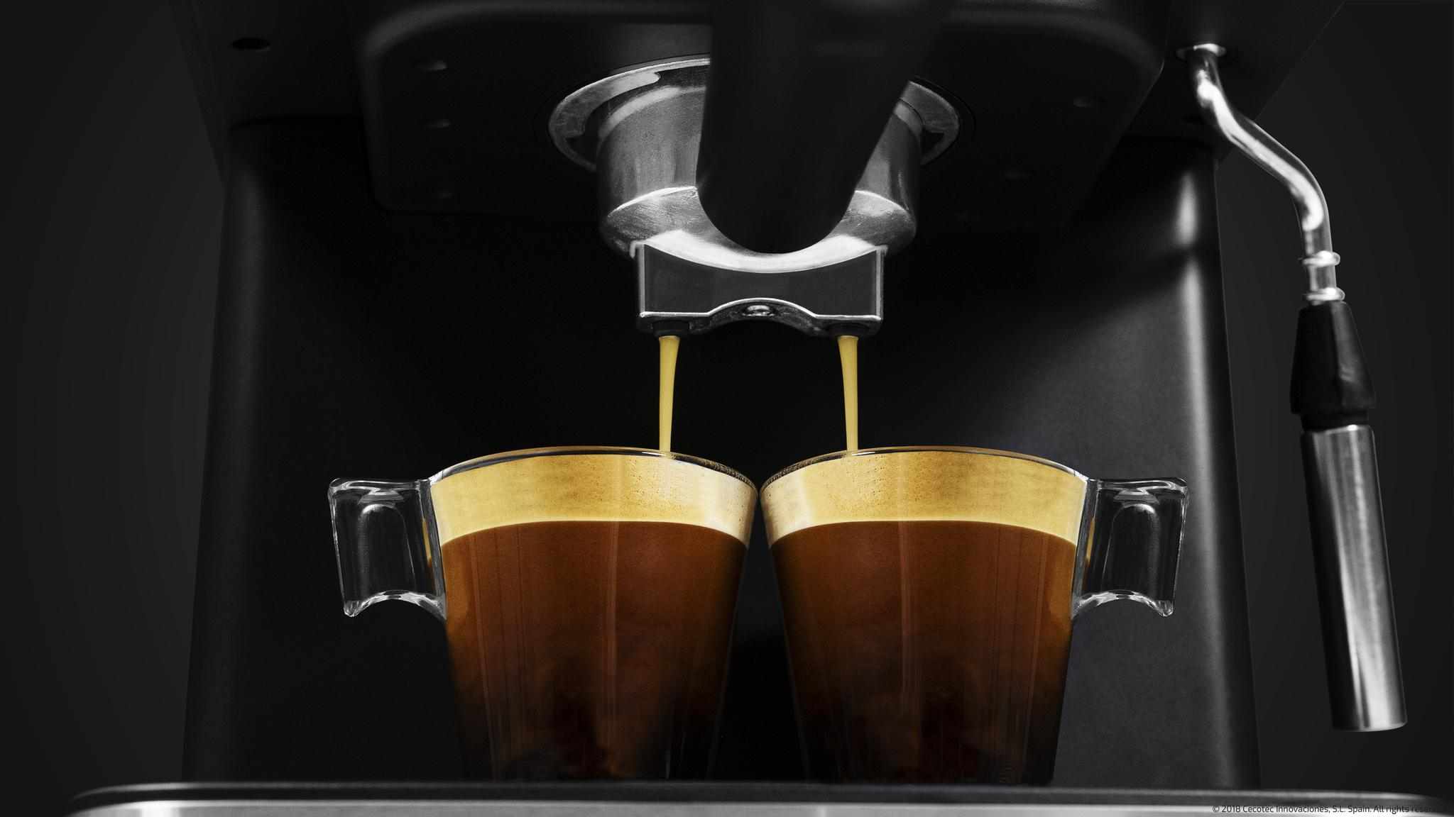 Cafetera llenando dos tazas transparentes con café fresco.