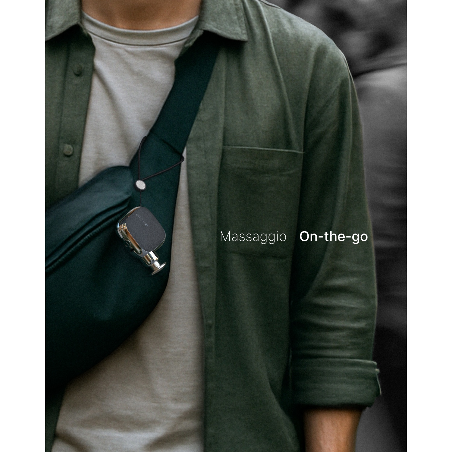 Una persona con camicia verde indossa una borsa scura con un piccolo massaggiatore, con testo Massaggio On-the-go.