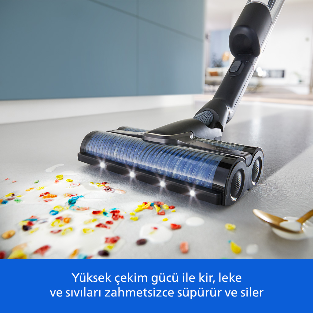 Bir elektrikli süpürge mutfak zeminindeki dökülmüş mısır gevreği ve sütü temizliyor.