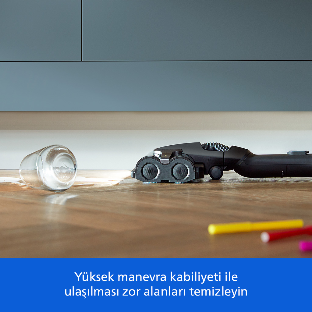 Siyah bir süpürge, devrilmiş bir bardak ve kalemlerin yakınında ahşap zemini temizliyor.