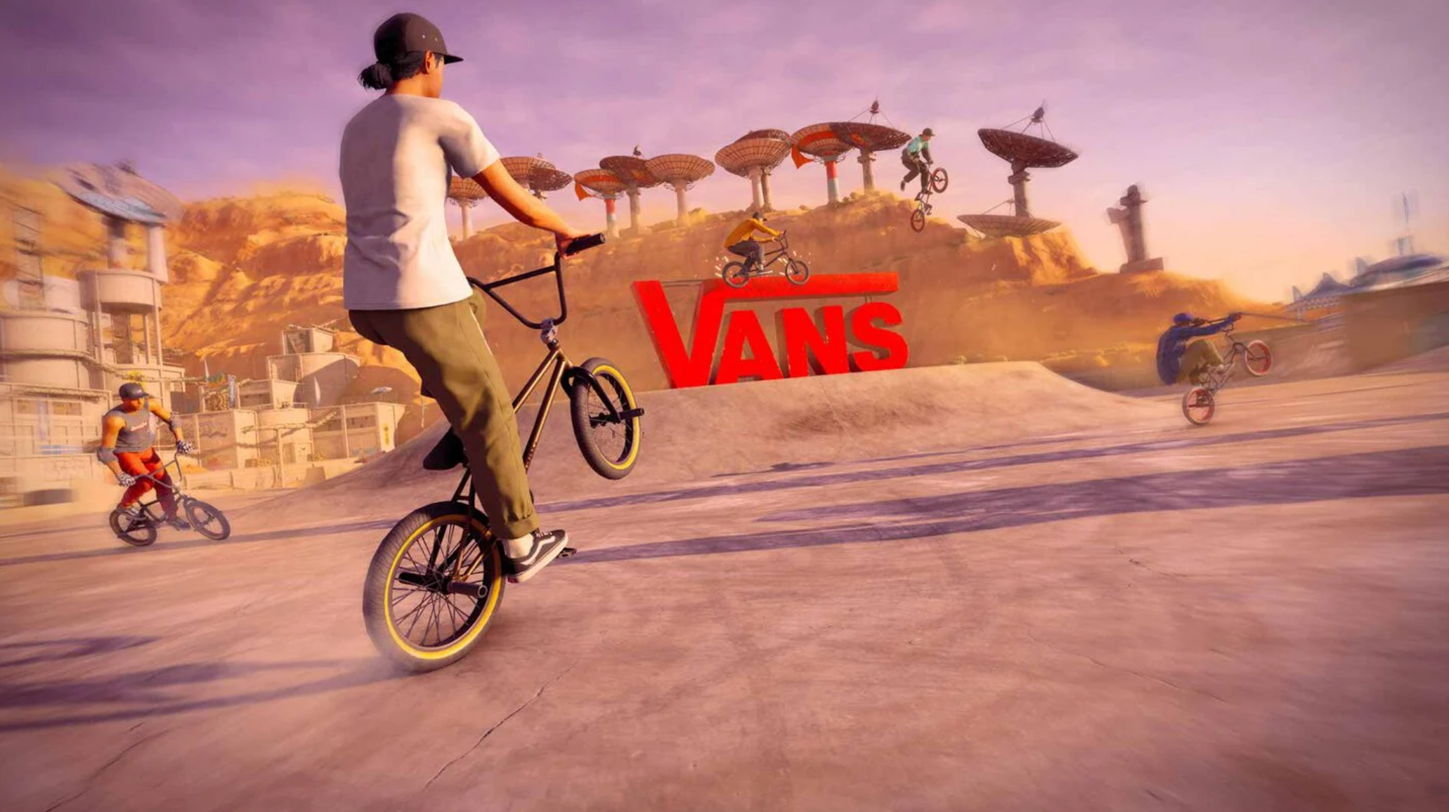 Varias personas realizan acrobacias en BMX frente a un gran logotipo rojo en un desierto.