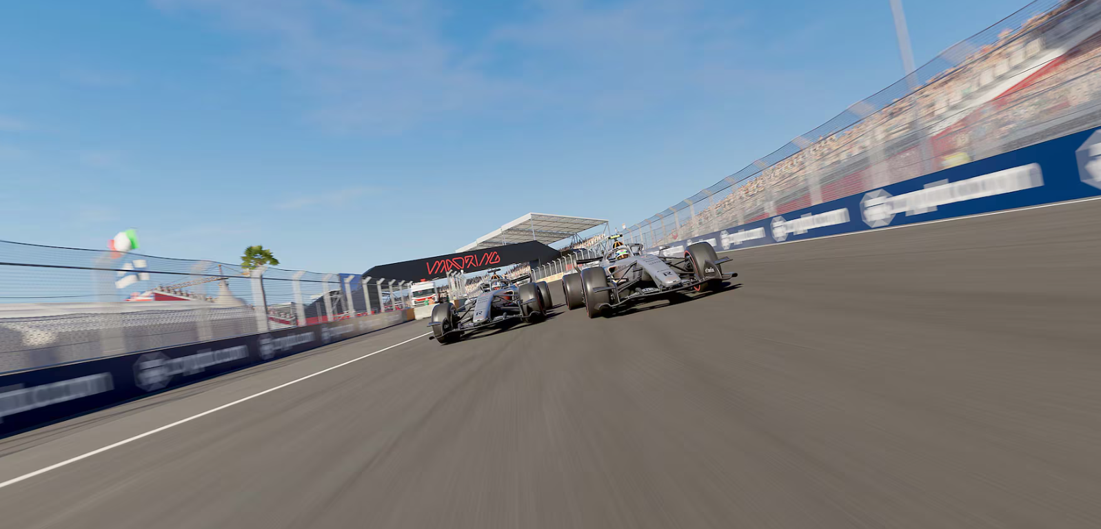 Dos coches de Fórmula 1 compiten en una pista soleada pasando por una tribuna.