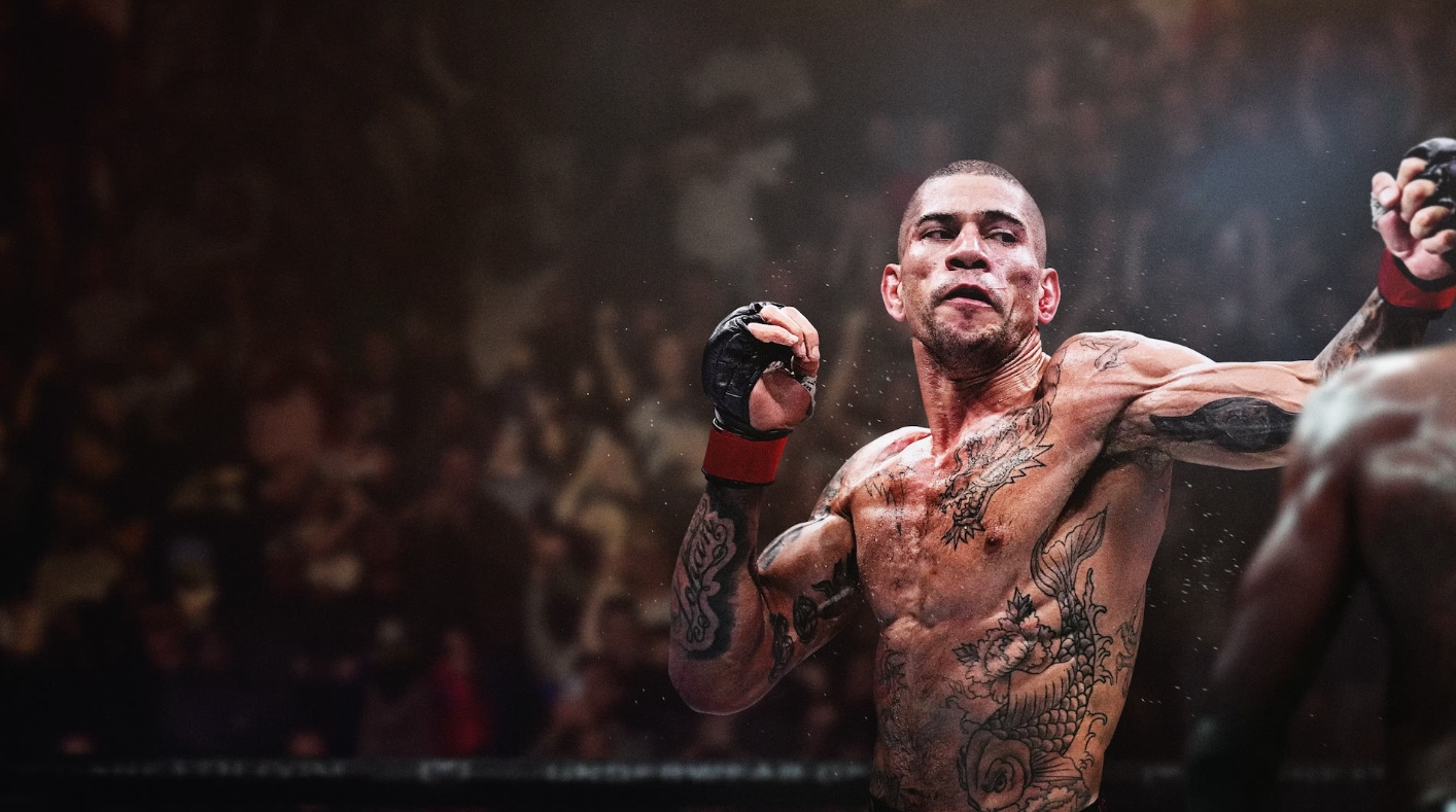 Un luchador de MMA tatuado lanza un golpe en un ring oscuro y concurrido.