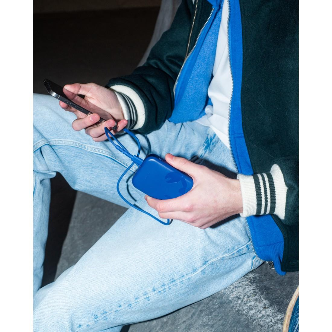 Eine Person sitzt und lädt ein Smartphone mit einer blauen Powerbank und einem Kabel auf.