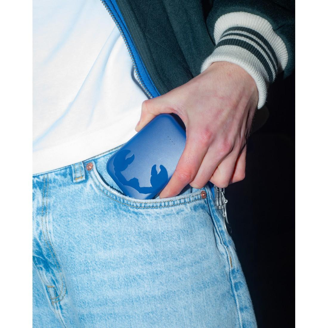 Eine Person in hellen Jeans steckt ein blaues Etui mit Krabbenmotiv in die Tasche.
