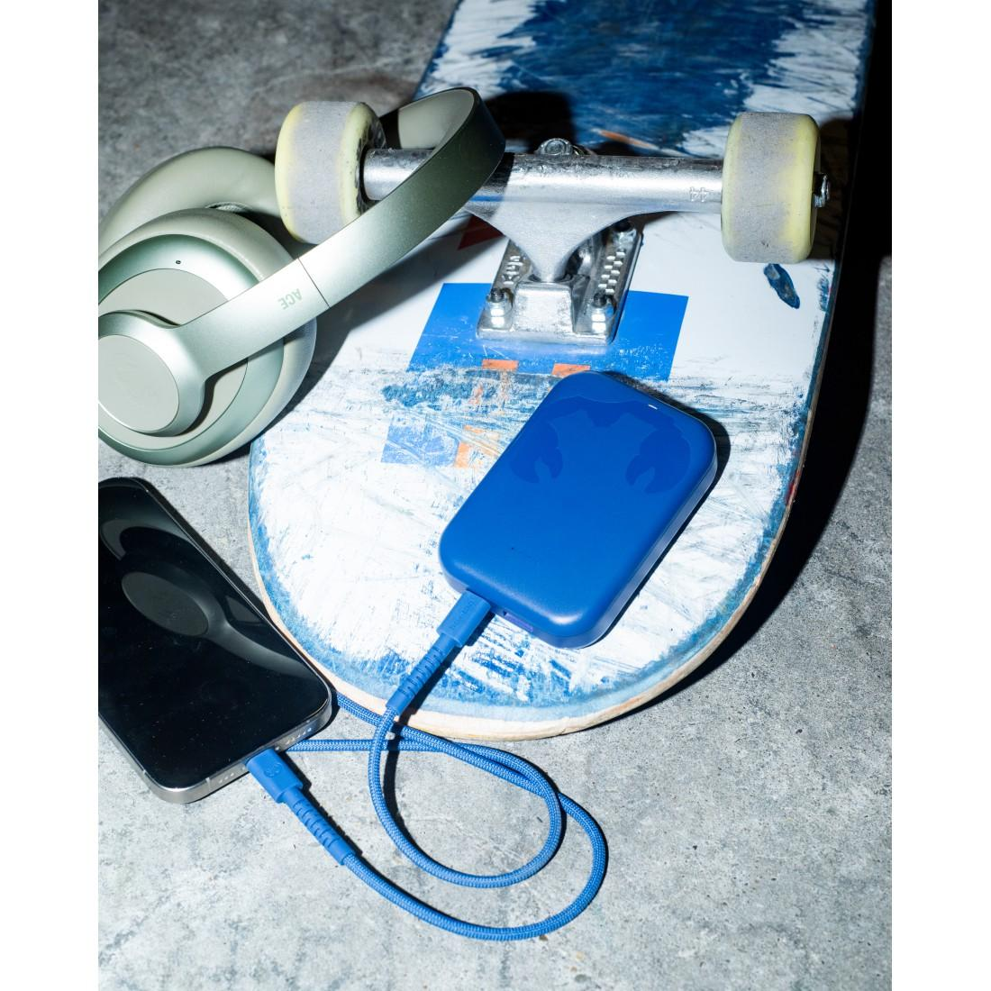 Ein Skateboard mit grünen Kopfhörern, einer blauen Powerbank, die mit einem Kabel an ein Smartphone angeschlossen ist.
