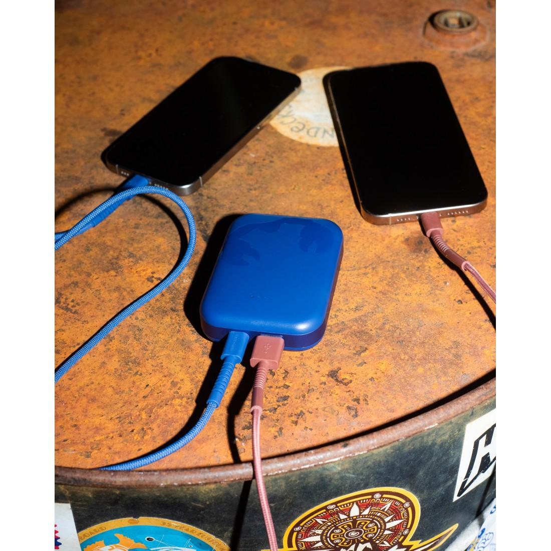 Zwei Smartphones laden an einer blauen Powerbank auf einem runden, rostigen Tisch.