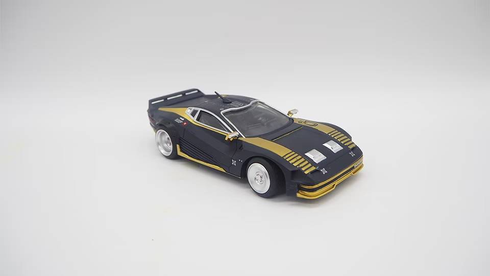 Un auto deportivo de juguete negro y dorado con ruedas blancas sobre fondo blanco.
