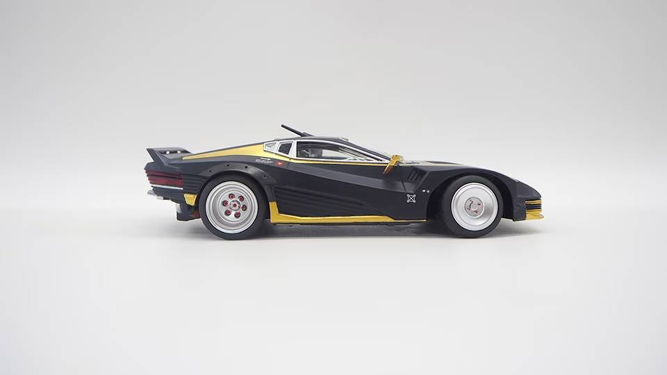 Un carro de juguete negro con detalles dorados se muestra de perfil sobre un fondo claro.