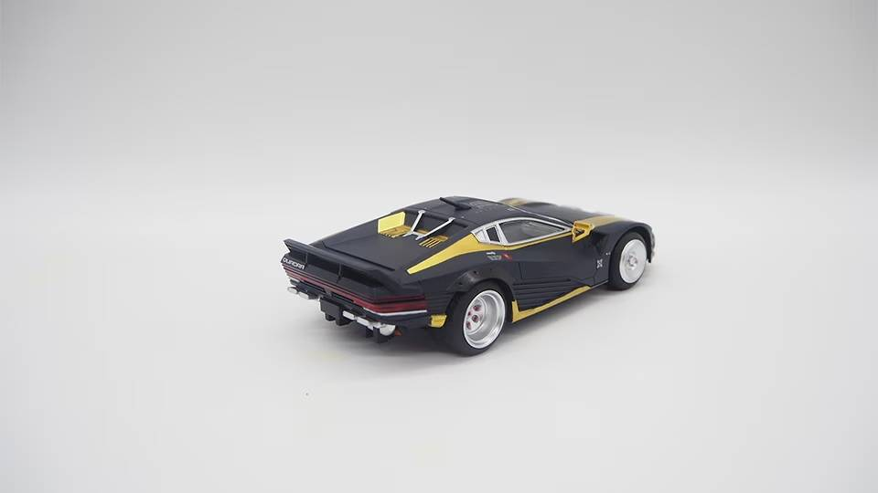 Un coche deportivo de juguete negro y dorado con alerón trasero sobre fondo blanco.