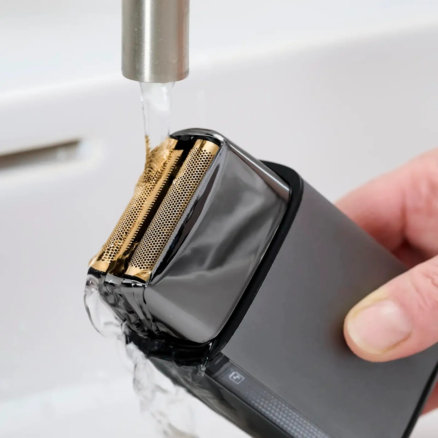 Egy elektromos borotva leöblítése folyó vízzel egy mosdóban.