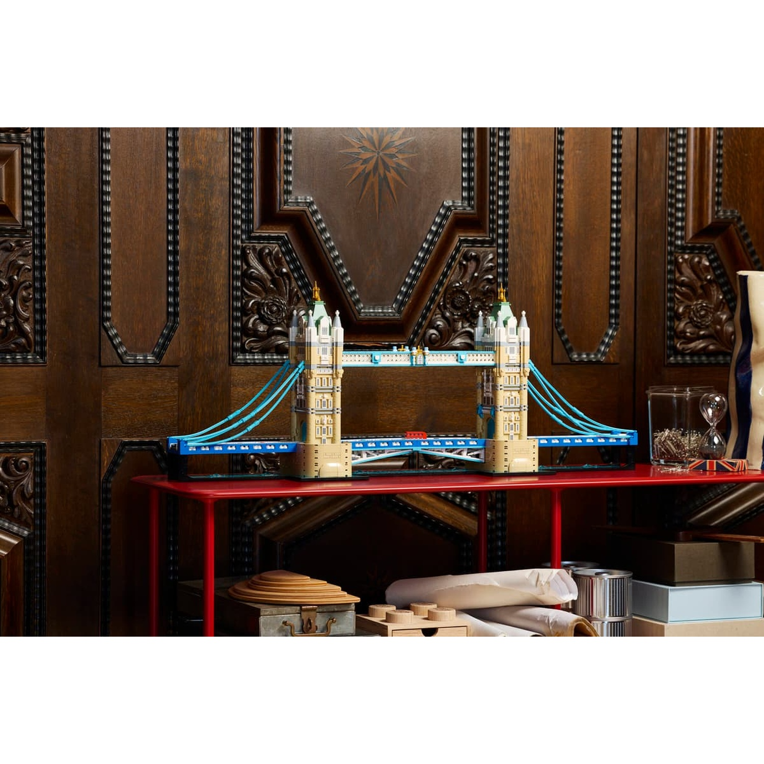 Un modello Lego del Tower Bridge su un tavolo rosso davanti a pannelli in legno.