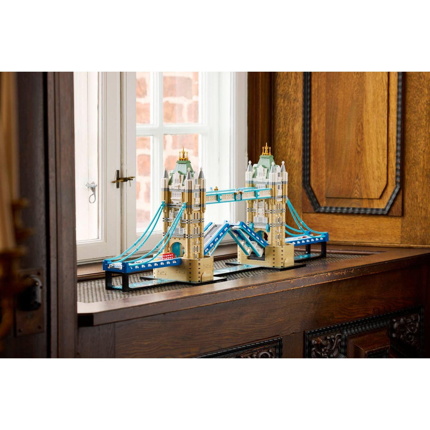 Un modello Lego del Tower Bridge si trova su un davanzale in legno davanti a una finestra bianca e pareti in legno.