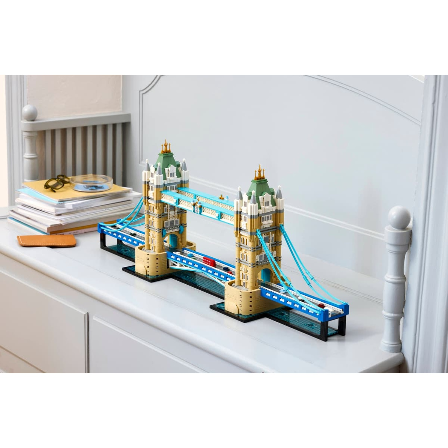 Un modello Lego del Tower Bridge si trova su una cassettiera bianca accanto a riviste impilate.