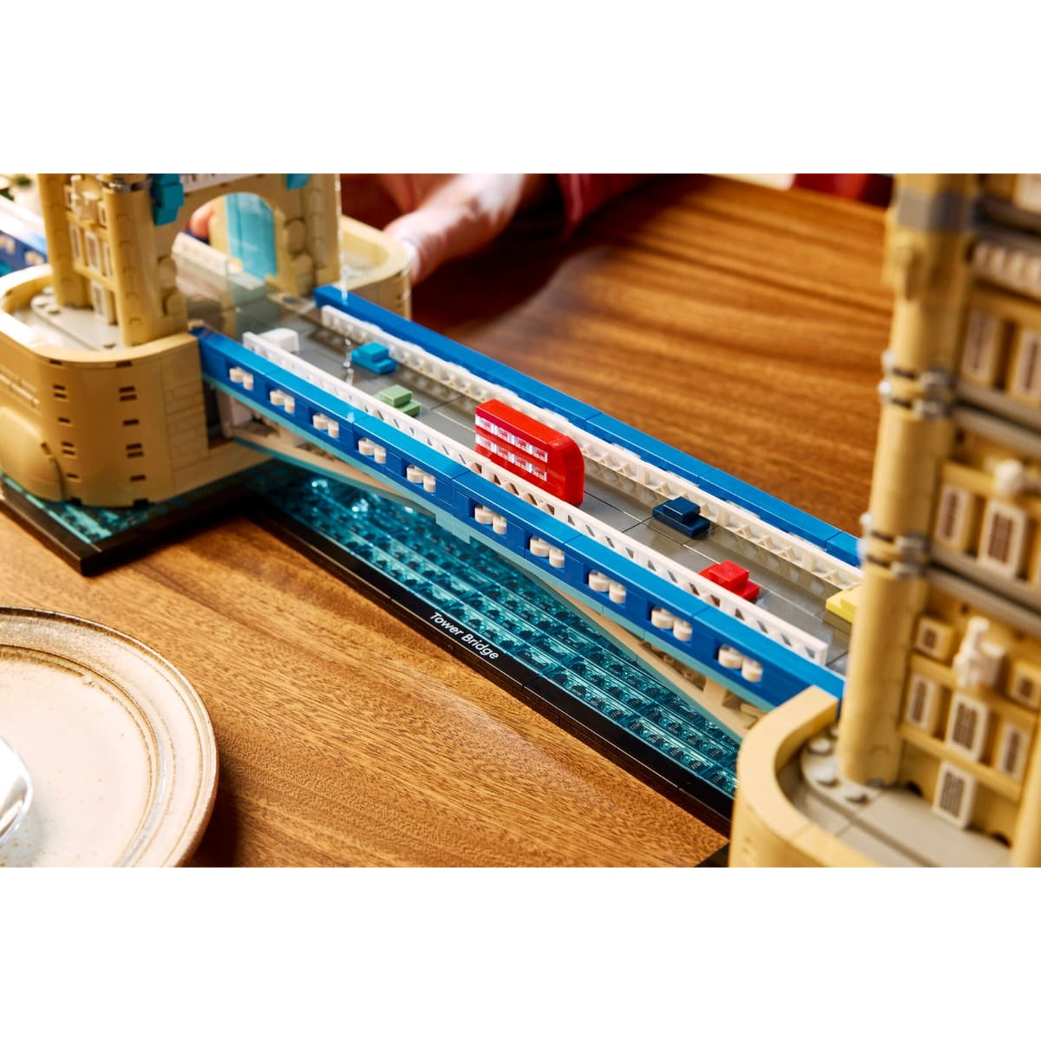 Un dettagliato modello Lego del Tower Bridge di Londra si trova su un tavolo di legno con piccoli veicoli.