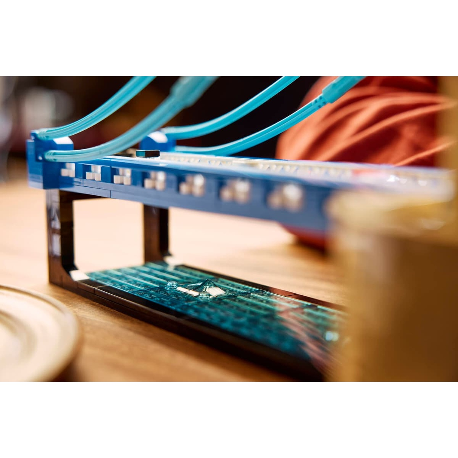 Un modello di ponte Lego blu e nero su un tavolo di legno con cavi di sospensione azzurri.