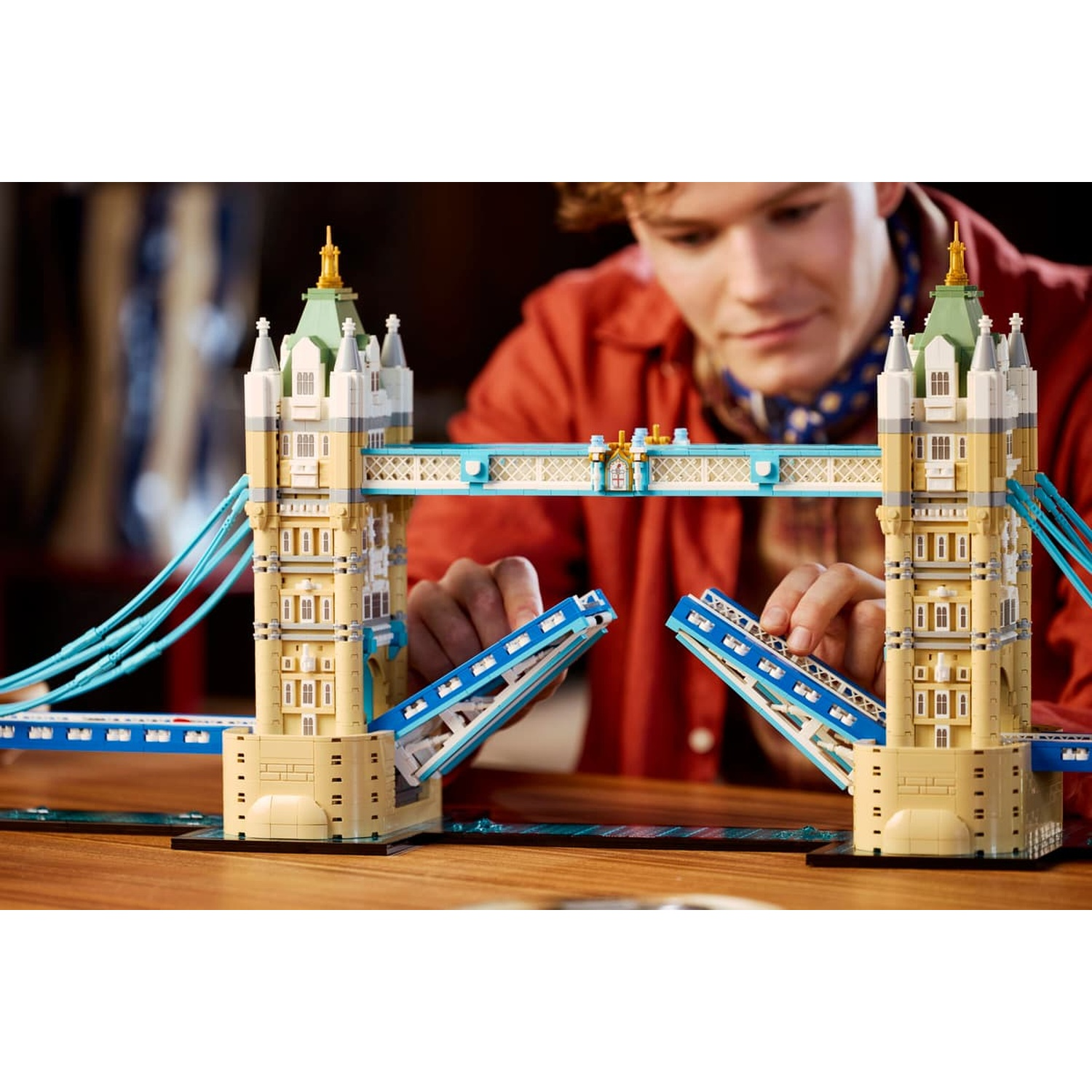 Un giovane costruisce un grande modello Lego del Tower Bridge su un tavolo di legno.